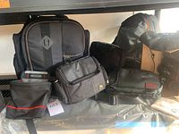 Multiple assorted camera bags, a MindShift brand backpack, and lens cases on a shelf.