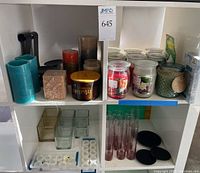 View of shelves with blue candles, brown candle, scented candle jars, battery operated tea light candles in holders, and glass bud vases.