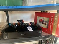 Canon Pixma MG6320 printer with stacks of ink cartridges and photo paper on shelf