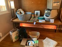 Entire cat supplies lot shown on wooden desk and floor including litter boxes, cat toilet seat, cat carrier, storage baskets, accessories, and cat fountain.