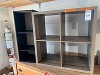 Two cubby shelves side by side showing the light brown gray laminate four-cubby bookshelf and the small black three-shelf case.