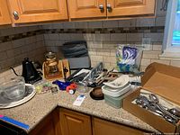 Wide view of countertop with all kitchen items showing electric kettle, glass carafe, utensils, Lazy Susan, silverware box, and container.