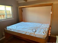 Wooden murphy bed frame in open (bed) position against wall