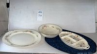 Full set displayed including large oval platter, bowl, divided serving tray on dark cloth, on white backdrop