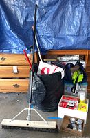 Overview of various cleaning tools including push broom, brushes, folded stools, and collapsible bin in a garage setting.