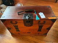 Top view of the wooden trunk showing black metal latch and side handles with key and metal tools on top.