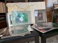 Lot of photography prints with matting and string lights draped over a board. Prints include nature scenes with green foliage and flowers.