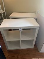 Pair of white IKEA cube storage shelves with four cubbies each, shown standing side-by-side on the floor.