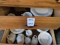 Drawer showing stacked white plates and coffee cups with handles below