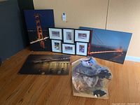 Full view of three large bridge photographic posters on foam board, six framed photos with white mats of bridges, and primate wall sticker on floor against wall
