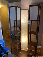 Set of three floor lamps: two wood with shelves and white panel shades, one tall fabric lamp.