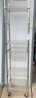 Full view of tall wire rack showing four shelves, wire basket drawer, hooks, and casters.