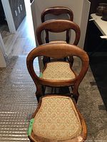 Three antique wooden chairs arranged in a row showing curved backs and upholstered seats with floral fabric.
