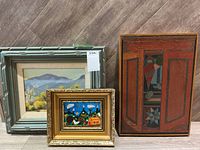 Group shot of three framed paintings leaning against wall on wood floor