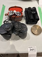 Three pairs of binoculars and a circular brass magnifying glass on a table.