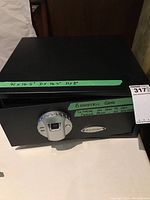 Front view of the black Barska biometric safe with green tape showing approximate dimensions labeled as 16.5" W x 14.5" D x 8" H.