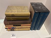 Full view of the nine hardcover books showing two stacks: one of six varied titles and one three-volume set from the Folio Society in blue covers with gold titles.