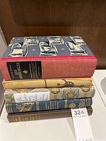 Five hardcover books stacked on a surface showing spines and partial covers