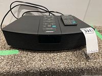 Front view of black Bose Wave Radio with remote on top, showing curved speaker grille and control panel.