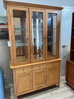 Full view of wooden china cabinet showing three glass doors in upper section and wooden drawers and cabinets below.