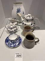 Full tea set including teapot, milk jug, sugar bowl, two rustic cups, and blue and white cup with saucer.