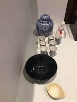 Wide shot of lot showing all ceramic items including ginger jar, figurine, cups, and bowls on a white table.