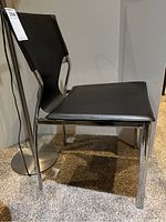 Black chair with metal frame and padded black seat and back viewed from the side on a carpeted floor.
