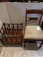 Photo showing wooden chair with carved backrest and upholstered seat next to wooden magazine rack on wheels