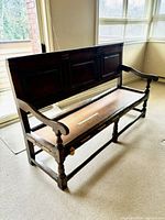 Full view of dark stained wooden church pew with paneled back, carved armrests, turned legs, no seat cushion