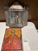 Tin display shrine with hinged doors open showing interior figurine and religious icon panel on surface