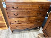 Front view of the wood dresser showing four drawers and brass handles, with visible surface wear and scratches.