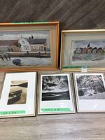 Five framed pictures arranged on the floor showing a mix of paintings and black and white photographs.