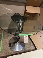 Full view of glass table with chrome base and stool on carpeting, showing dimensions and condition.