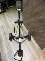 Front view of the Bag Boy golf cart showing the handle, wheels, and frame, placed on a wooden floor indoors.