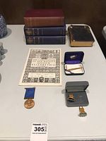 Photo showing the same booklet and medal alongside a tie bar and two pairs of cuff links in presentation boxes.