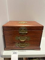 Front view of wooden jewellery box with brass latch and two drawer handles.
