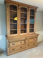 Full view of large wooden farmhouse style buffet and hutch set in natural wood finish with glass doors and drawers.