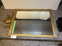 Full view of the rectangular mirror showing reflective surface and gold-toned frame with ornamental details at the top.