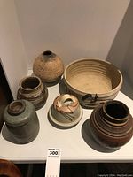 Overview of six pottery items on a white surface, showing various shapes including bowl, vases, and a covered dish.