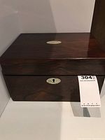 Closed wooden writing box showing dark finish, front keyhole with white oval plate, and slight wear.