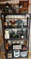 Full view of black metal shelving unit with various decorative and electronic items arranged across four shelves.