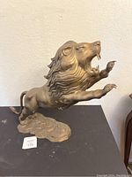 Lion statue showing left side view with raised paws and open mouth, mounted on a decorative base.