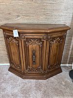 Front view of the wooden entry way cabinet table showing carved decorative panels and door with handle.
