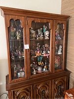 Full view of wooden display cabinet containing multiple clown figurines across three glass-front shelves