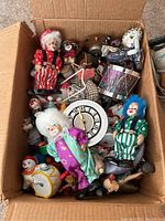 Box filled with various clown figurines, mostly porcelain, featuring colorful costumes and painted faces.