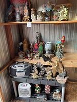 Wide view of three shelves filled with assorted decorative items including animal and human figurines, glassware, and small electronics.