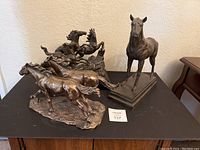 Three bronze horse statues on black table: two galloping horses statue, two rearing horses statue, and one standing horse statue on base.