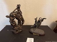 Two bronze cowboy and bull rider statues showing full figures and bases