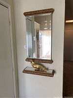 Full view of mounted wall mirror with decorative top and bottom frame, and ledge with gold peacock figurine