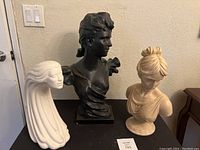 Photo showing three female bust statues placed on a surface against a wall, depicting their relative size and appearance.